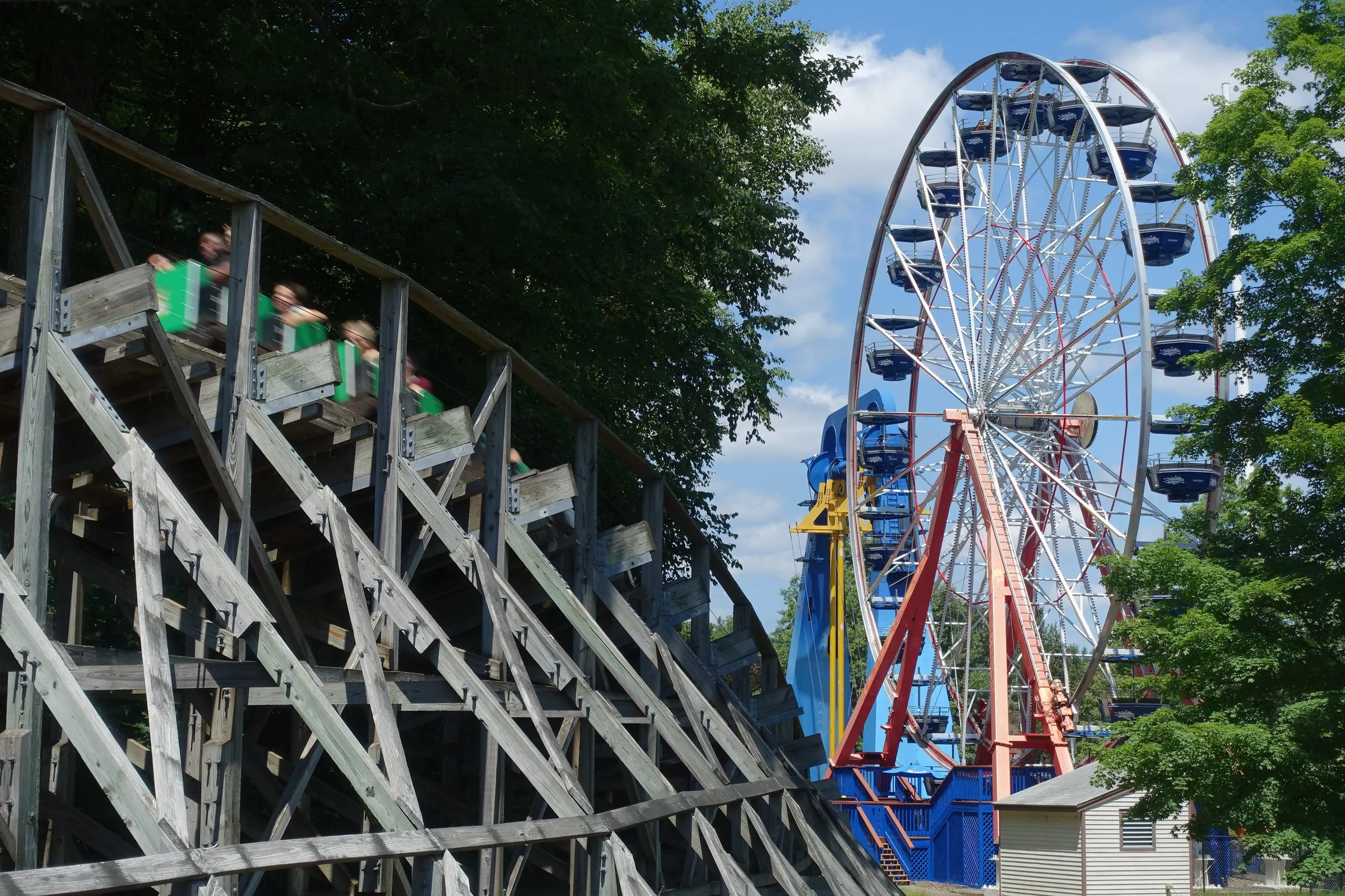 A train on the Boulder Dash wooden roller coaster passing the Ferris wheel at Lake Compounce on a summer day