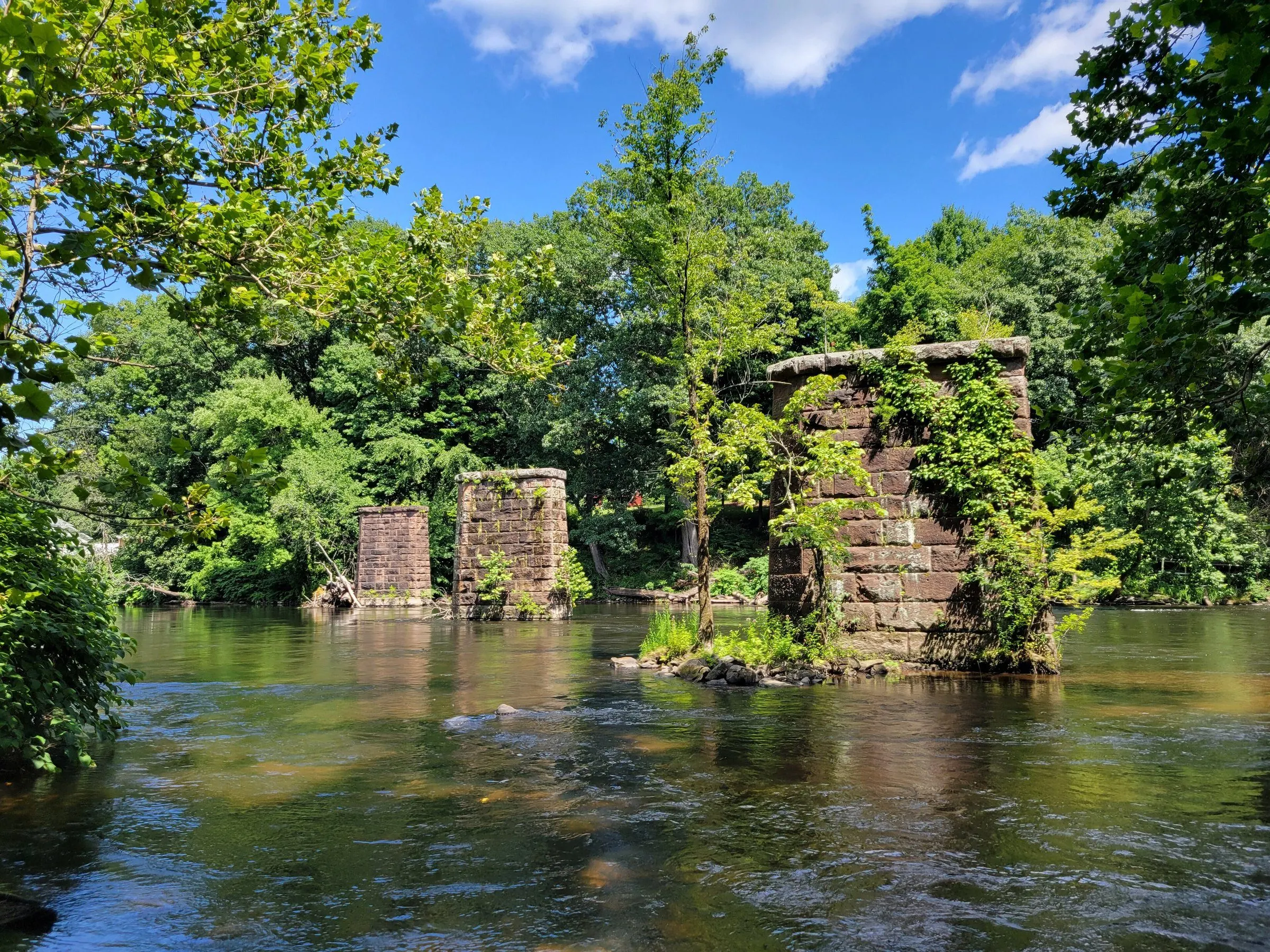 Old stone railroad piers standing in the Farmington River at Tariffville, surrounded by summer trees
