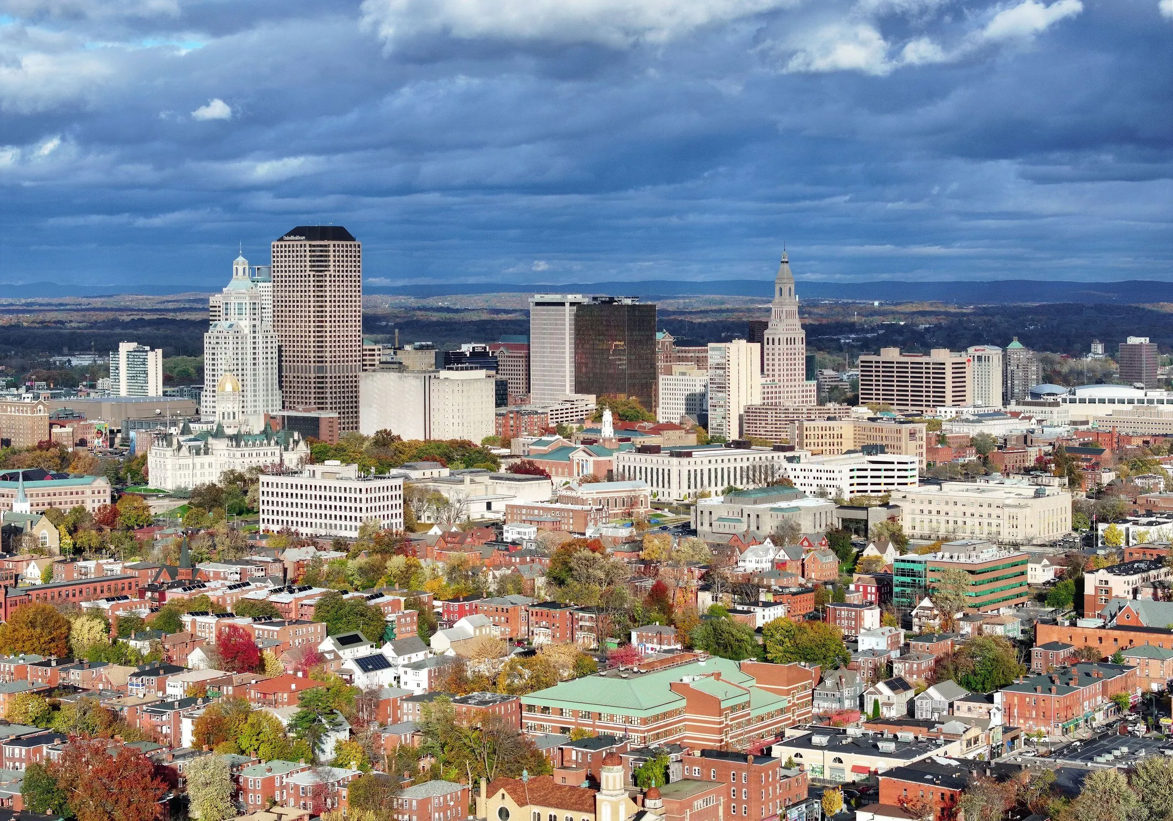 Downtown Hartford's towers above red-brick neighborhoods and autumn trees, under a dramatic sky