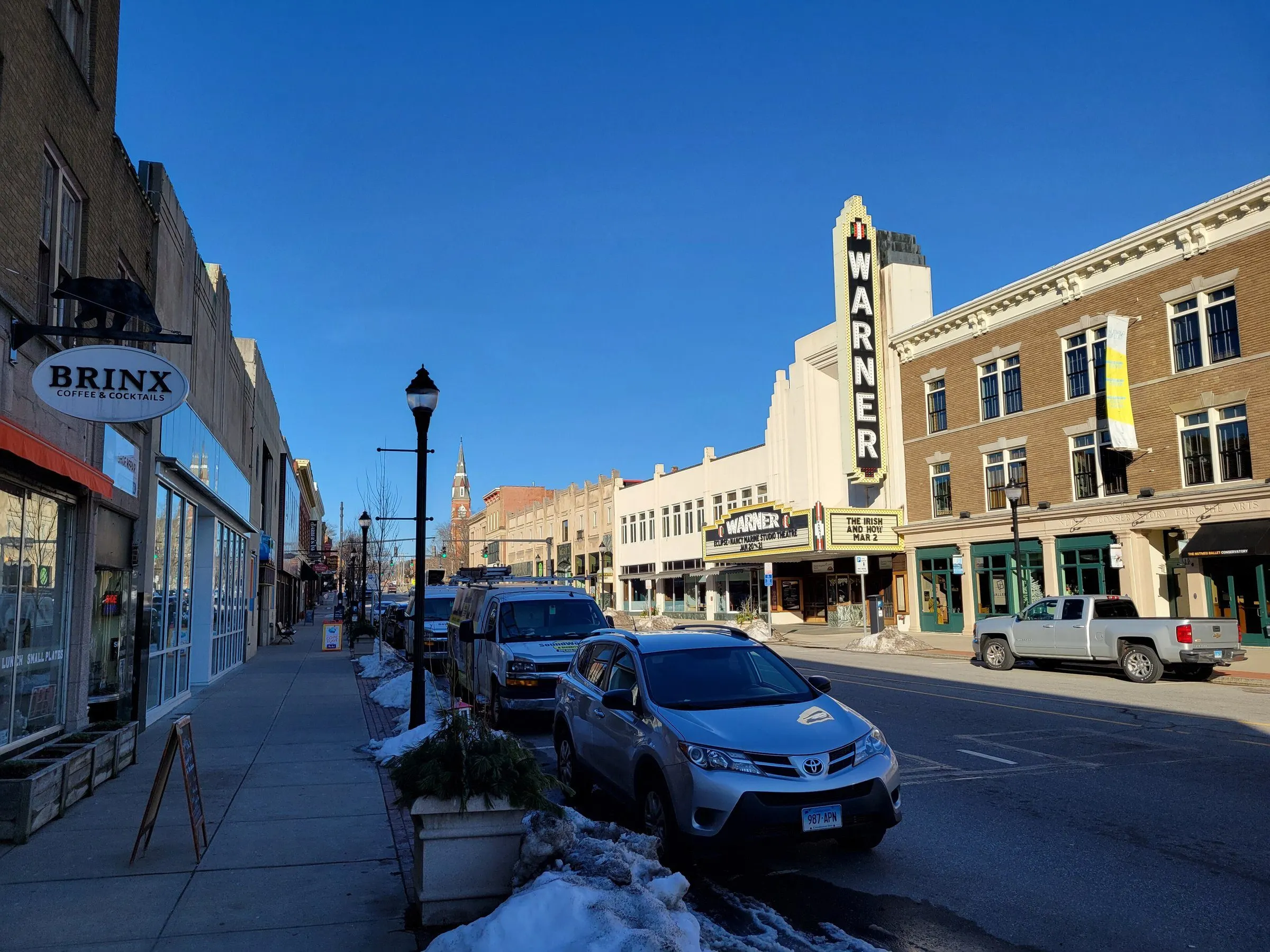 Main Street in downtown Torrington with the Art Deco Warner Theatre marquee and brick commercial blocks under a blue sky