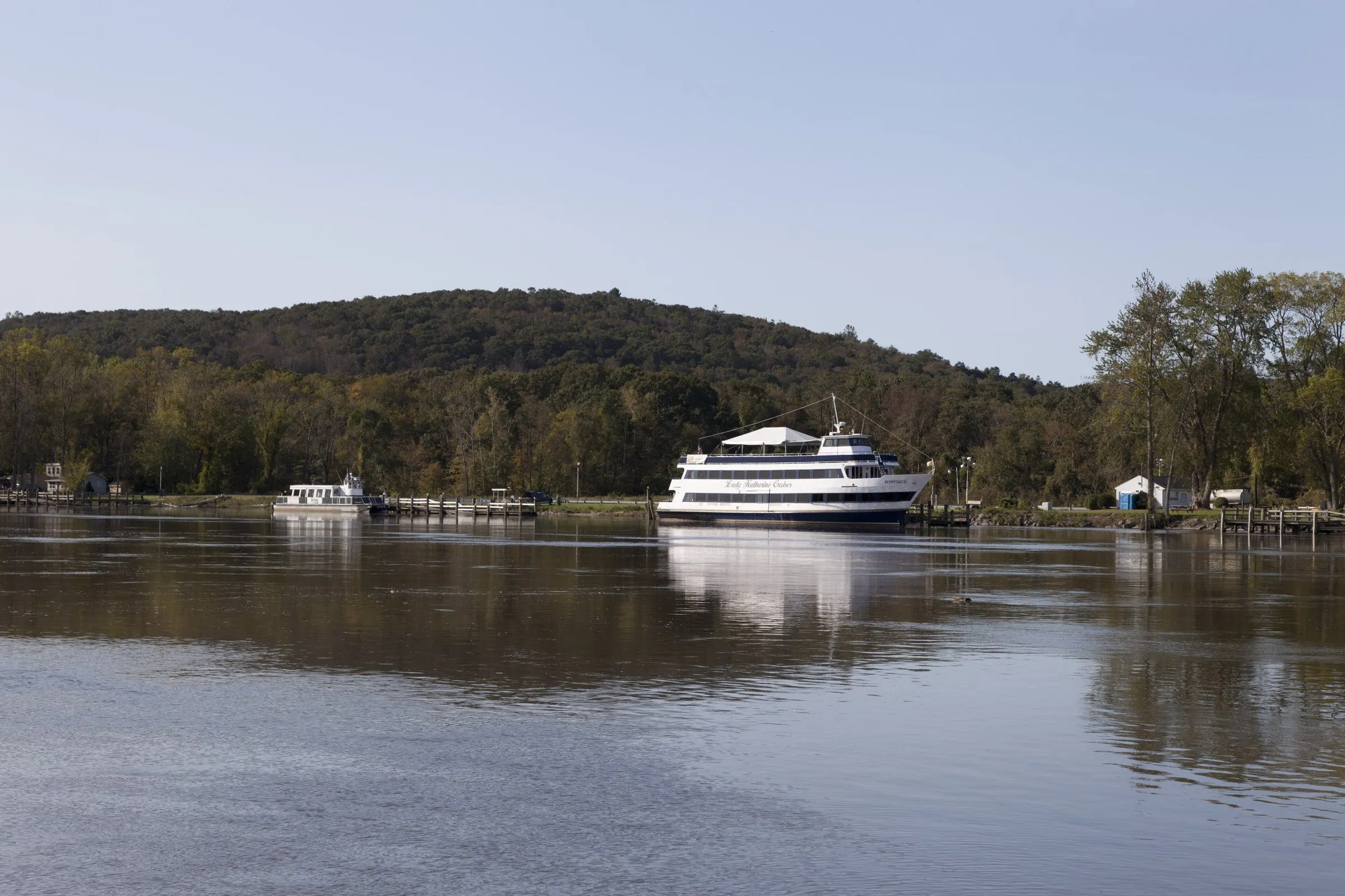 A white riverboat moored on the calm Connecticut River at East Haddam, below wooded hills