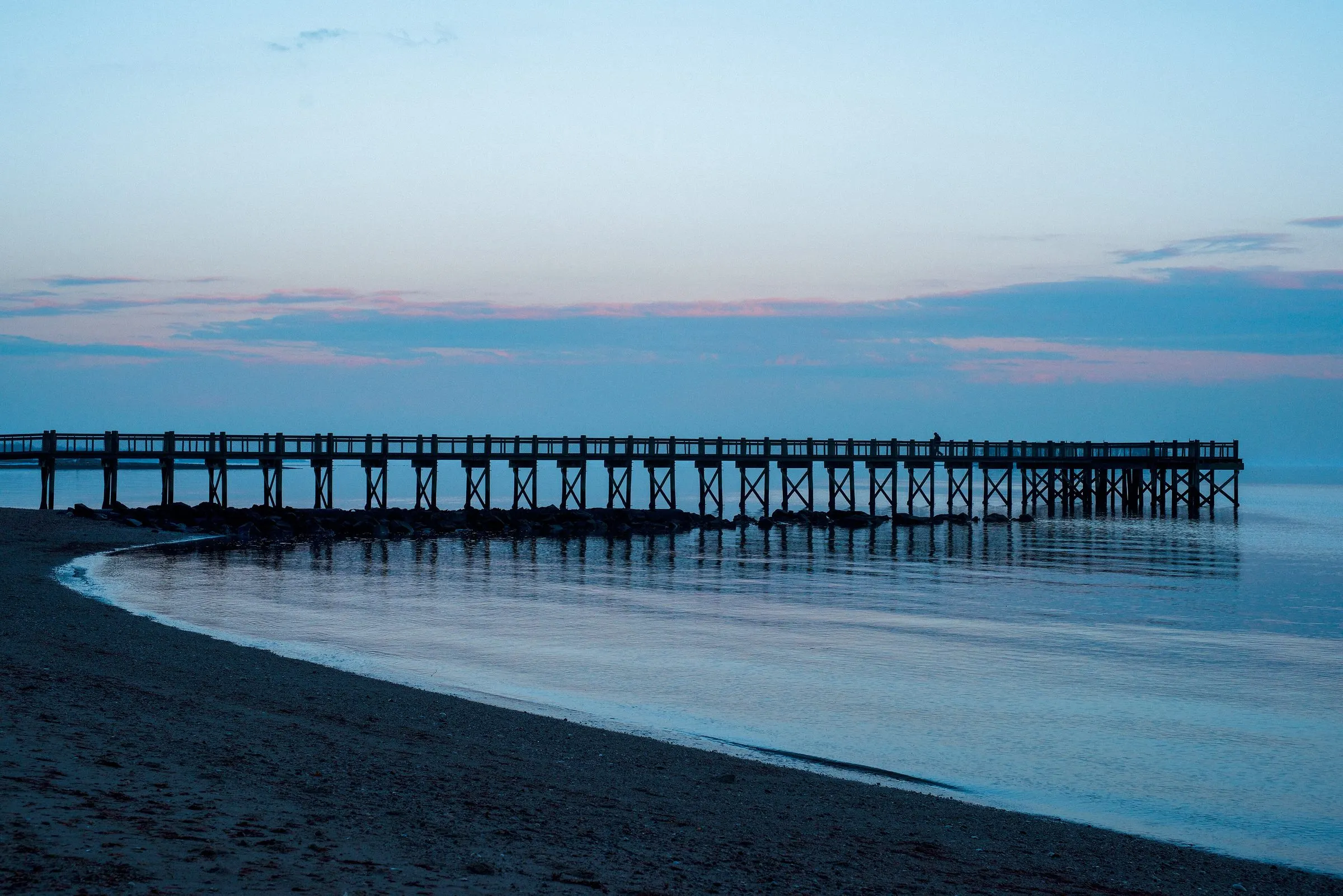 The long pier at Walnut Beach in Milford at dusk, reflected in calm water