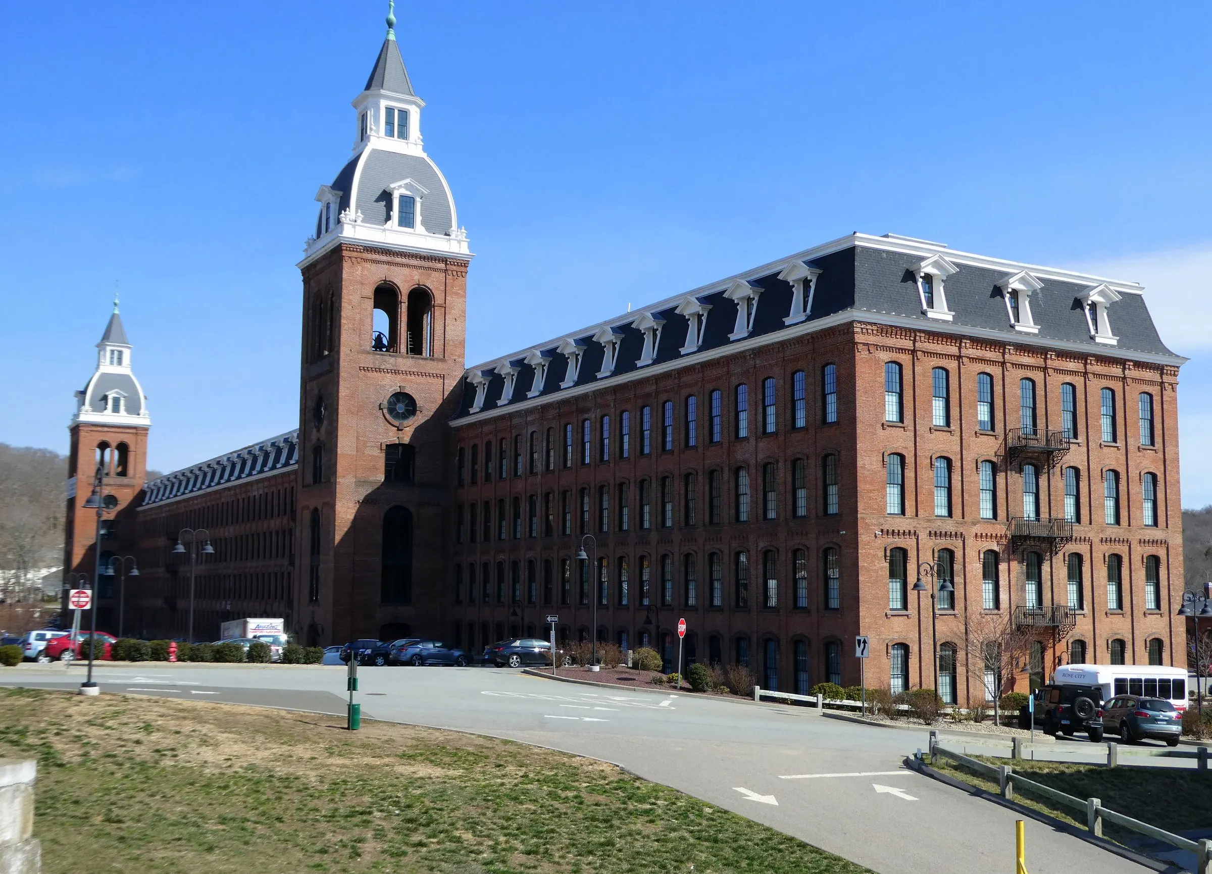 The long brick facade of Ponemah Mills with its mansard roof, dormers and clock tower under a clear blue sky