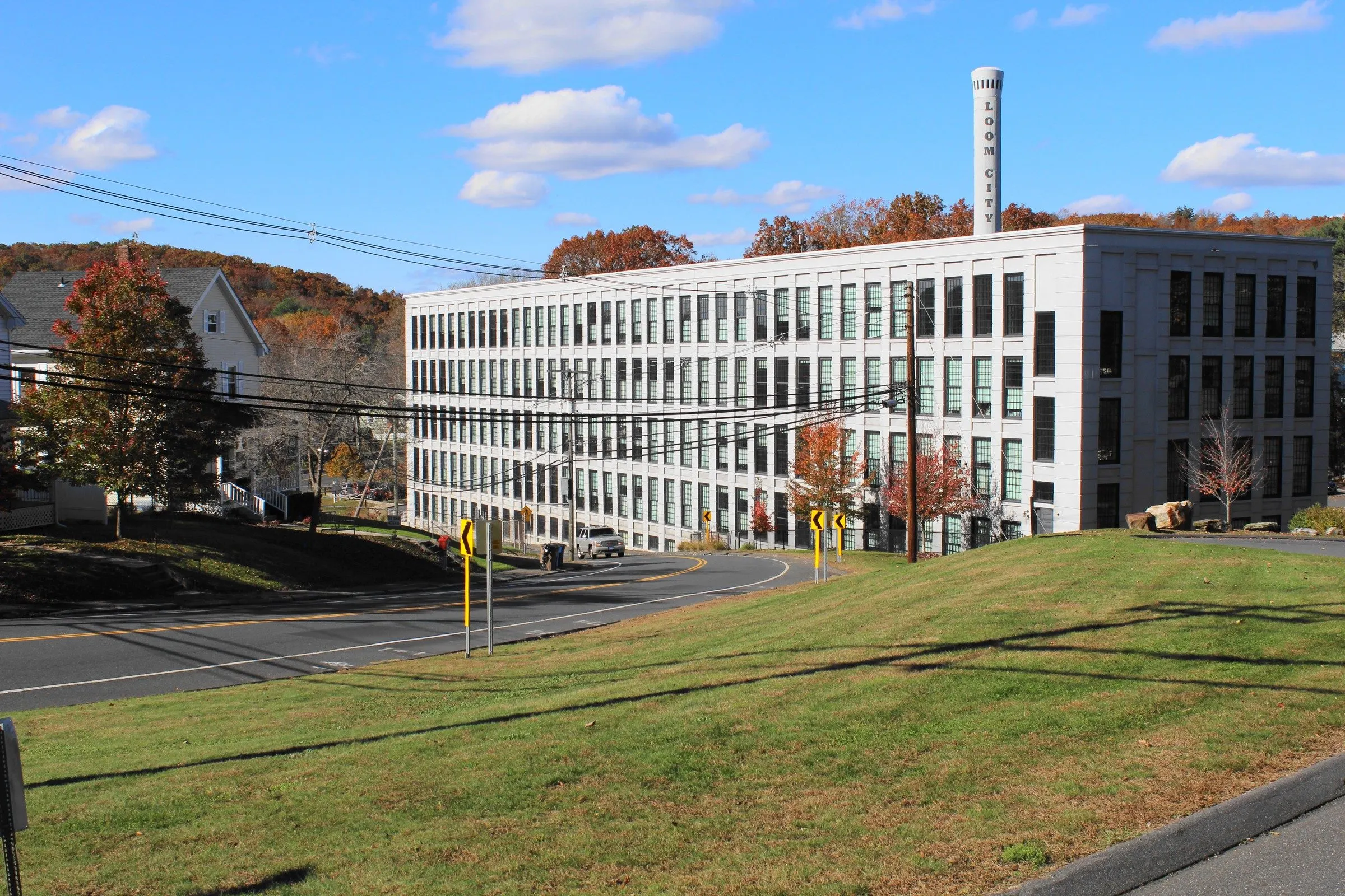 The white 1906 Minterburn Mill in Rockville, now Loom City Lofts, with its smokestack and autumn trees under a blue sky